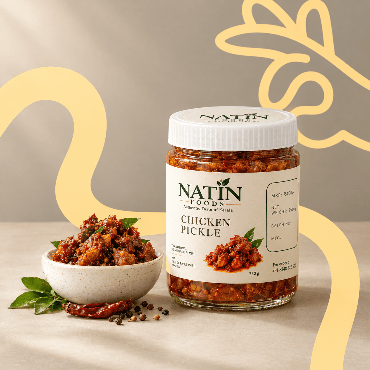 Glass jar of Natin Foods chicken pickle with a white cap and printed label, standing beside a stone bowl of pickle garnished with curry leaves; dried red chillies and peppercorns are scattered on the beige surface